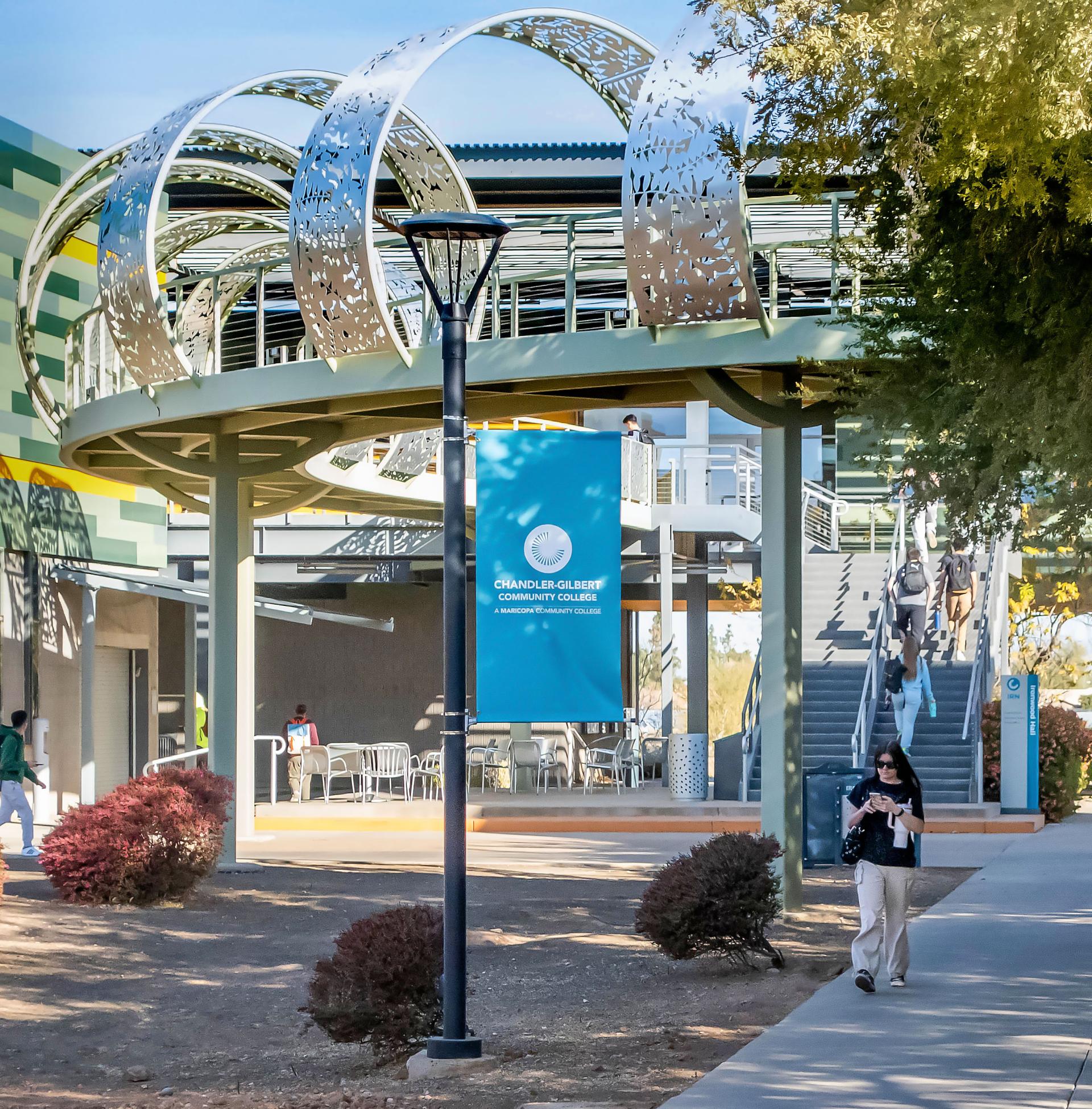 Pecos Campus features a bridge with a student walking underneath and another student descending the bridge stairs.